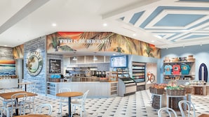 A cafe with a tropical mural, a coffee menu, and a variety of seating options.