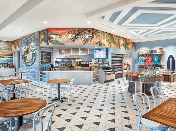 Una cafetería con un mural tropical, un menú de café y diversas opciones de asientos.