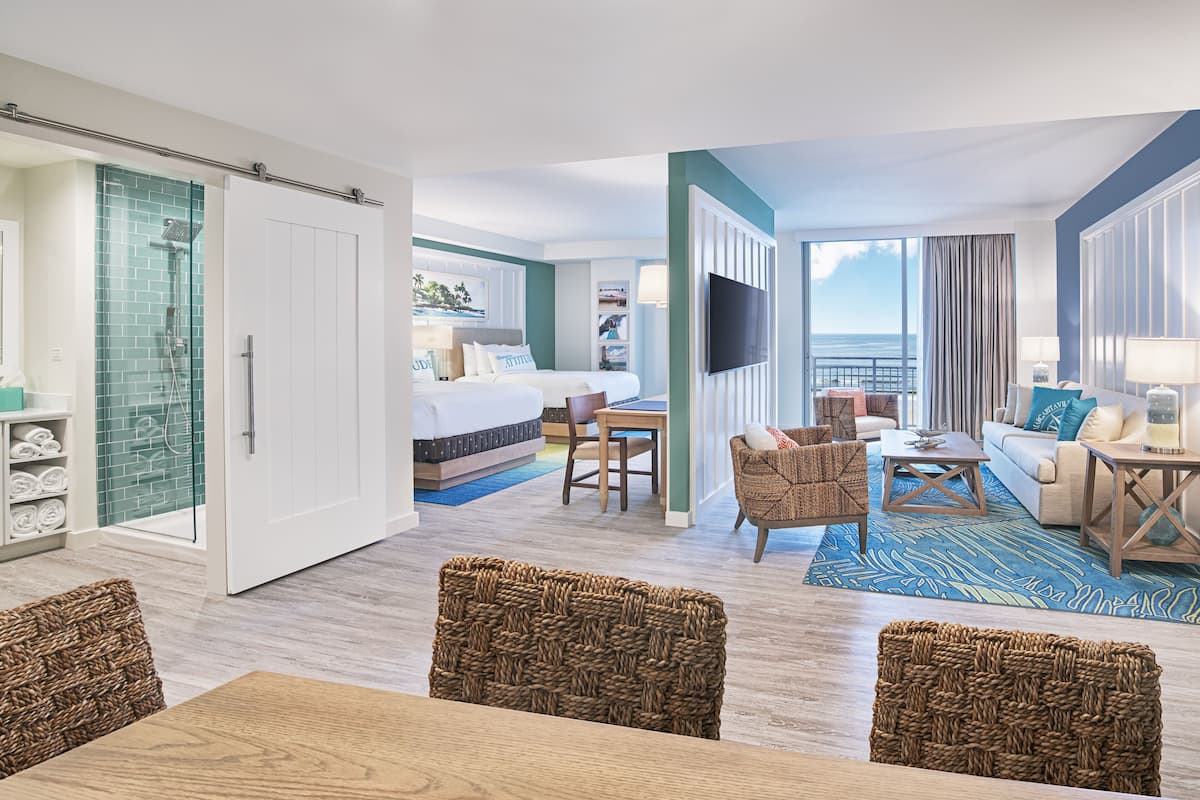 A hotel room with a bed, a desk, a TV, a balcony with curtains, and wicker furniture.