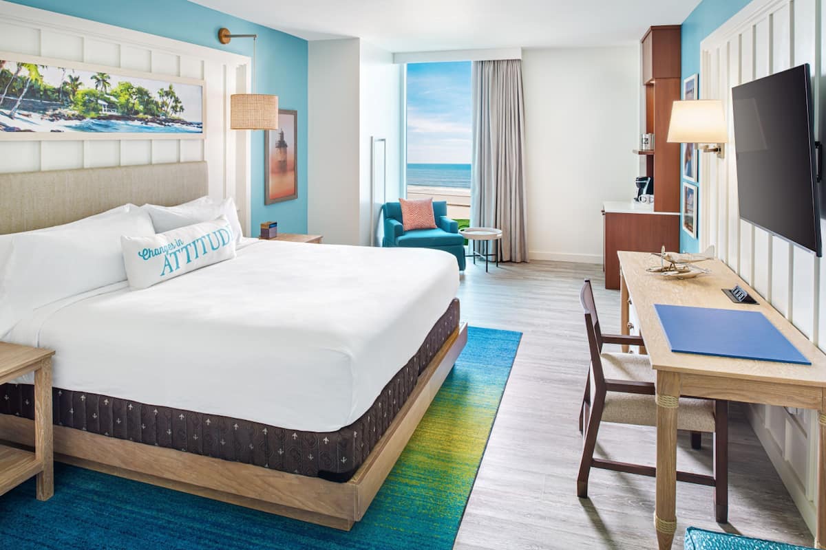 A hotel room with a large bed, a desk, a television, and a view of the ocean.