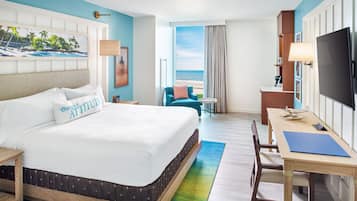 Quarto de hotel com uma cama grande, uma escrivaninha, uma televisão e vista para o oceano.