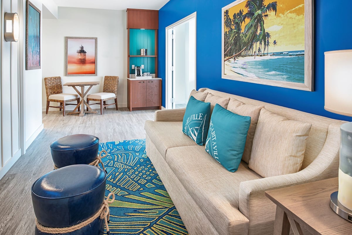 A living room with a blue wall, a sofa with teal cushions, a coffee table, and a painting of a beach scene.