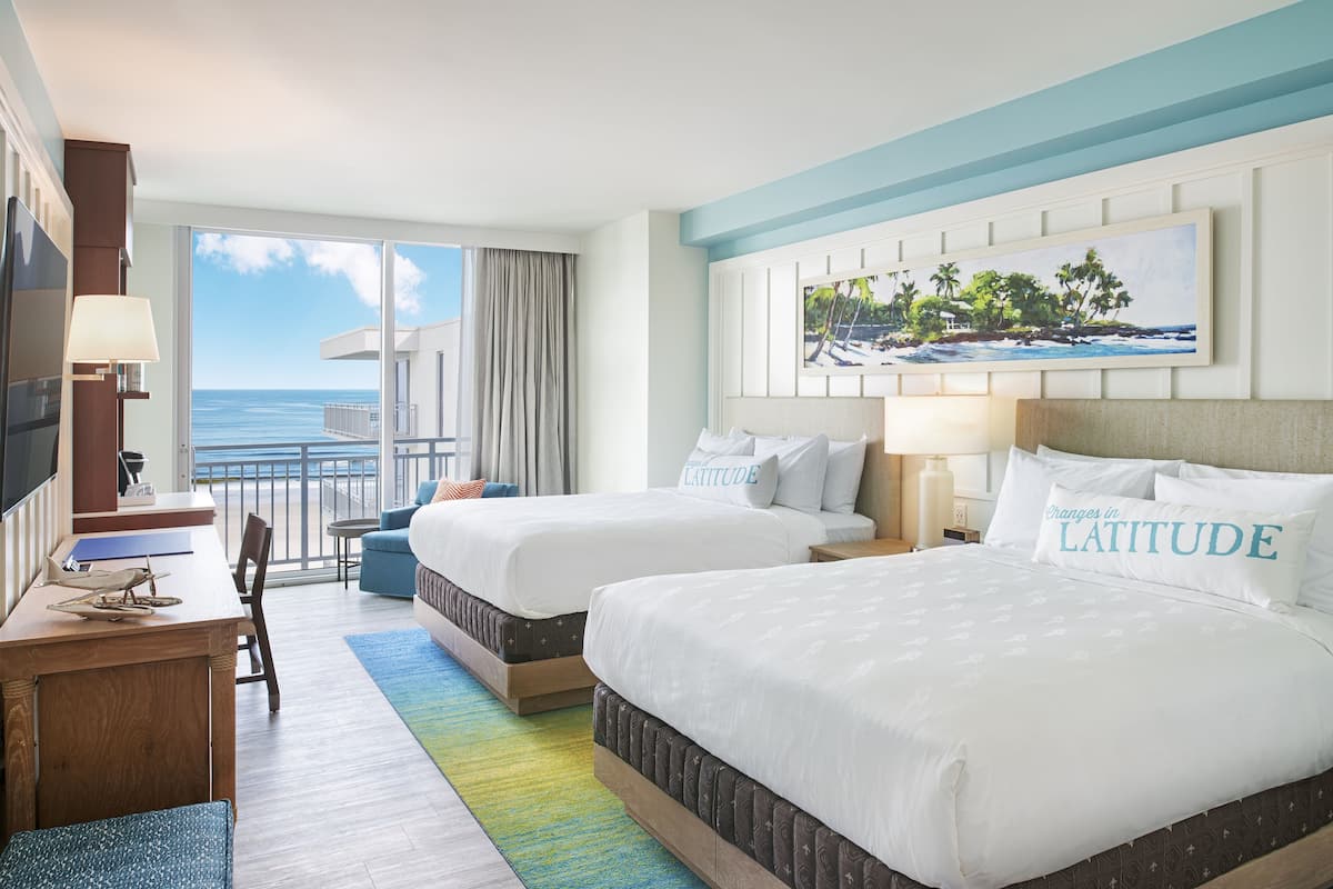 A hotel room with two beds, a desk, and a view of the ocean.