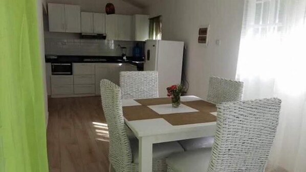 A dining area with a white table and chairs, a vase with flowers, and a kitchen in the background.