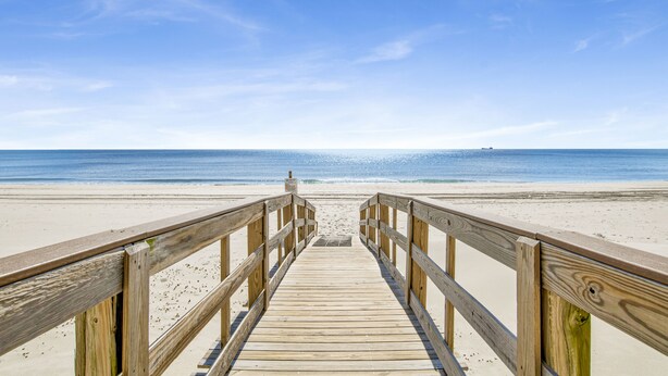 A wooden boardwalk leading to a beach with a clear sky.