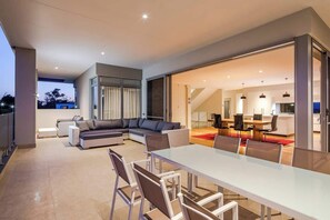 Un moderno salón con una mesa de comedor de cristal, un sofá modular y una cocina al fondo.