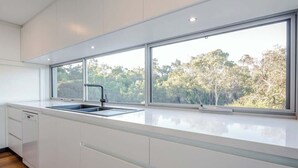 A modern kitchen with a large window, white cabinetry, and a stainless steel sink. - La Vacanza—Luxe Spacious Home with Ocean Views (Dunsborough)