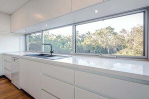 Una cocina moderna con un ventanal grande, muebles blancos y un lavamanos de acero inoxidable.