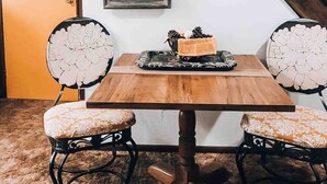 Un coin repas avec une table en bois et deux chaises rembourrées ornées de motifs floraux. Un cadre contenant la lettre « V » et une plaque portant l’inscription « Famille » sont accrochés au mur.