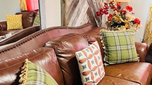Un canapé en cuir marron avec trois coussins, un mur en bois à motifs chevrons, une lampe et un vase de fleurs.