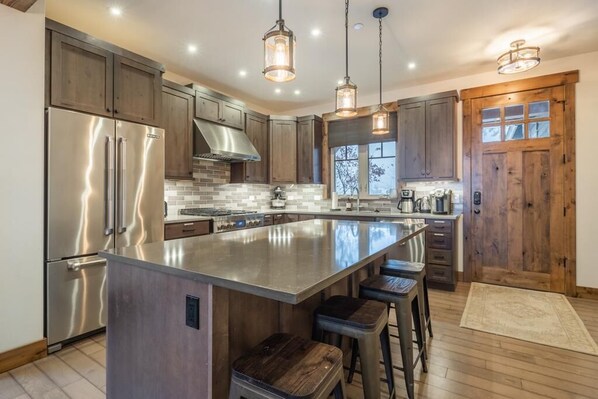 A modern kitchen with stainless steel appliances, a large island with bar stools, wooden cabinets, and pendant lighting. - Family Retreat w/ Suncadia Pool Access (Cle Elum)