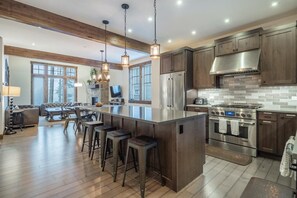 Une cuisine moderne dotée d’un grand îlot central, d’appareils électroménagers en acier inoxydable et de meubles de rangement en bois.