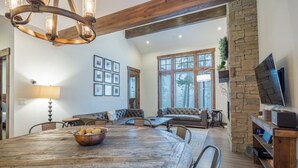 A spacious living area with a large wooden dining table, a comfortable seating arrangement, a stone accent wall, and a television. - Family Retreat w/ Suncadia Pool Access (Cle Elum)