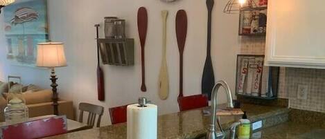 A kitchen with granite countertops, a stainless steel sink, a dish drying rack, and a clock on the wall.