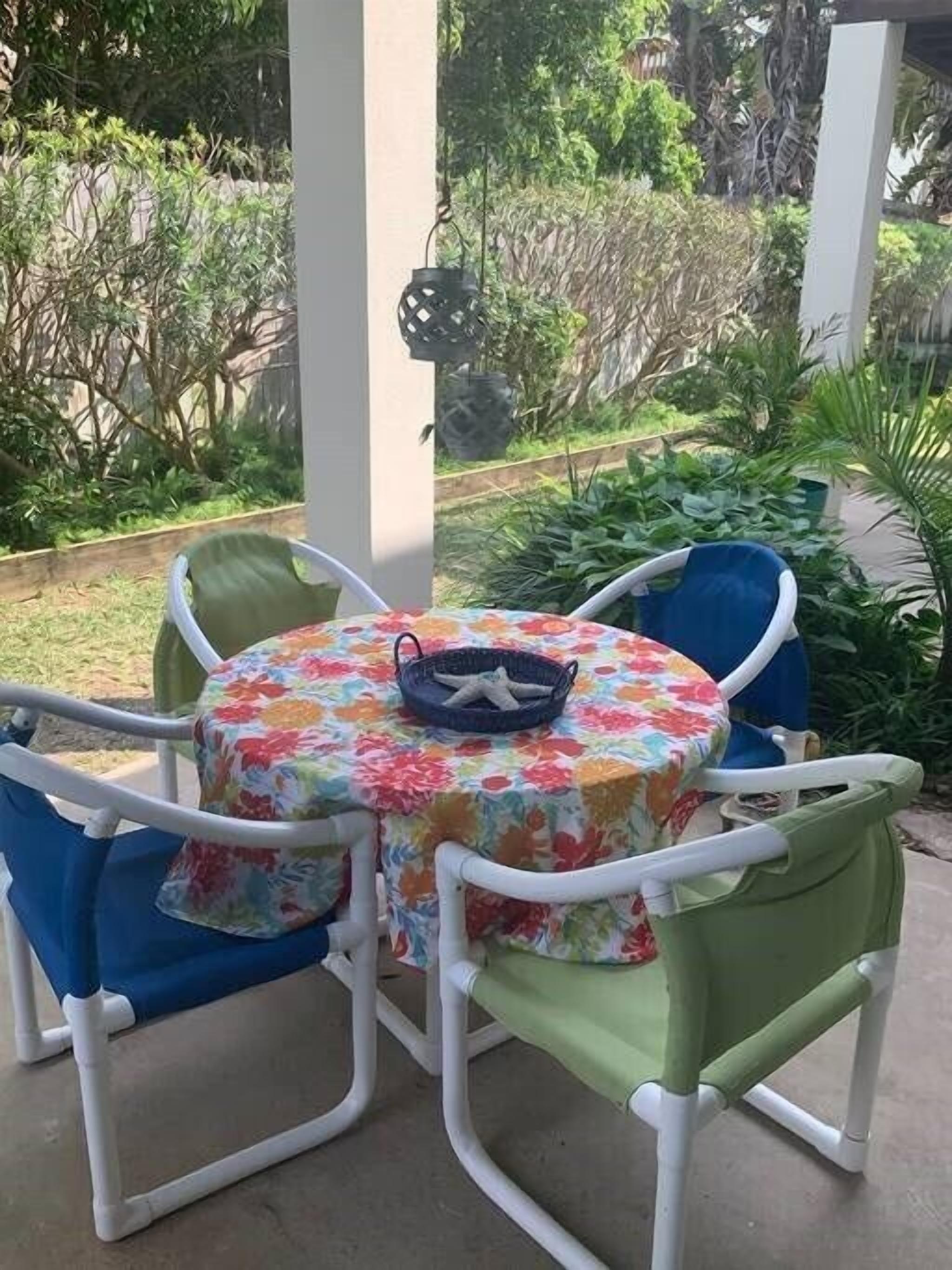 Una mesa redonda con mantel floral, rodeada por cuatro sillas con cojines de distintos colores.