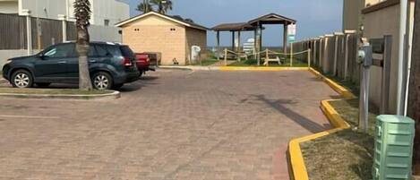 A paved driveway leading to a building with a covered entrance, palm trees, and parked cars.