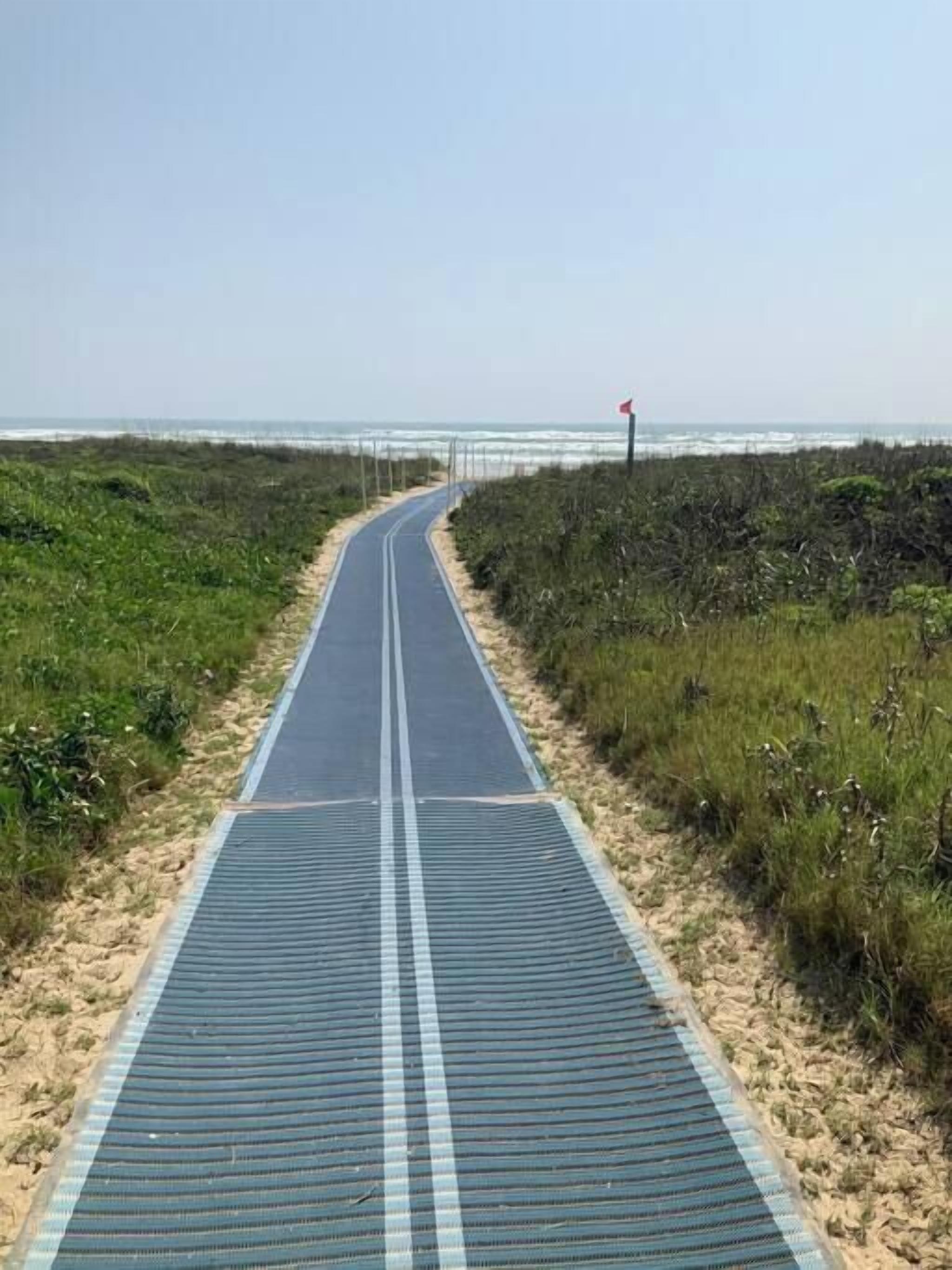 A paved pathway leading to a beach with a red flag marker.