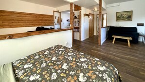 Een slaapkamer met een bed, houten hoofdbord, een bankje, een dressoir en een spiegel.