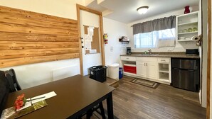 Een kleine keuken met witte kastjes, een koelkast van roestvrij staal en een houten wand.