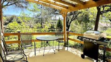 Eine überdachte Terrasse mit Grill, Sitzgelegenheit und Blick auf eine grüne Landschaft.