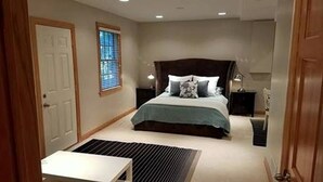 Une chambre à coucher avec un grand lit, une table de chevet, une commode, une fenêtre avec des stores et une porte.