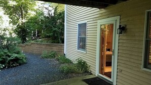 Une maison avec une allée en gravier, une terrasse en bois et une porte donnant sur une pièce avec une fenêtre.