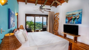 Un dormitorio espacioso con una cama grande, un ventilador de techo, un televisor sobre un mueble de madera y un cuadro de barcos en la pared.