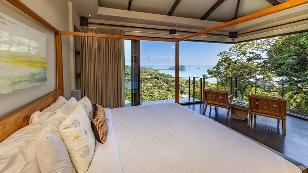 Un dormitorio con una cama grande, vistas al mar y un balcón con sillas.