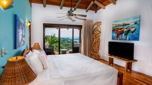 Un dormitorio espacioso con una cama grande, un ventilador de techo, un televisor sobre un mueble de madera y un cuadro de barcos en la pared.