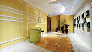 Un vestíbulo de hotel con una paleta de colores amarillo y blanco, un sillón verde, un espejo grande y una alfombra estampada.