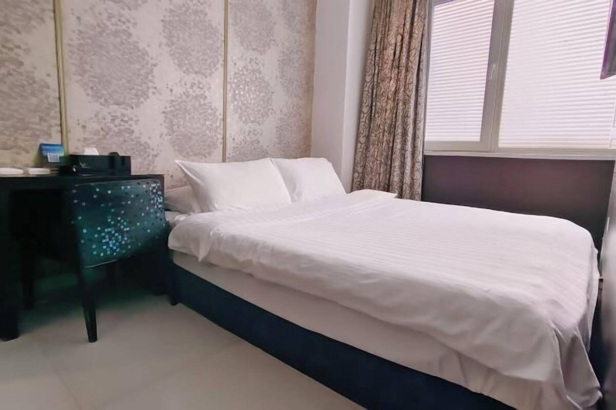 A bedroom with a bed, a desk, and a window with curtains.
