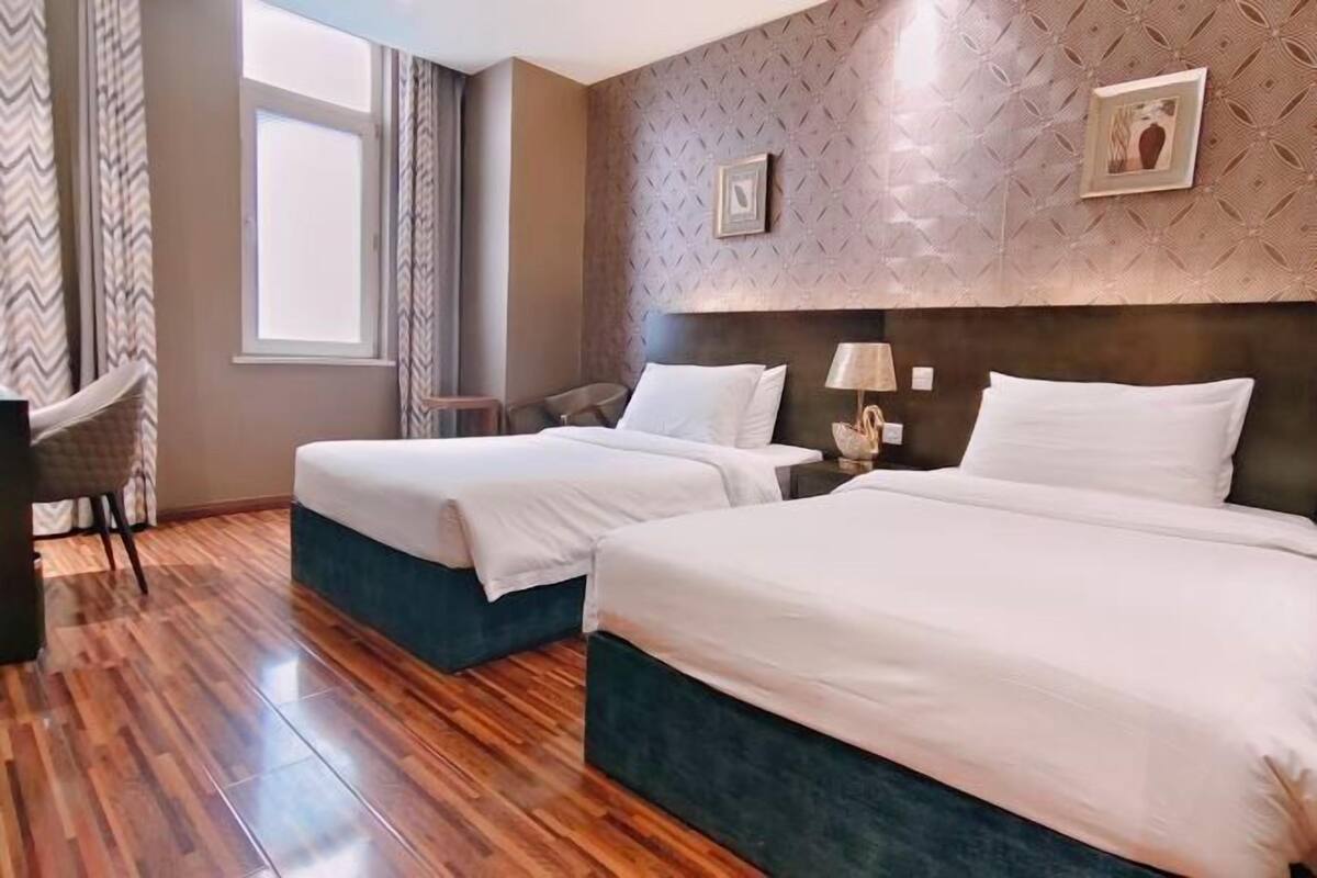 A hotel room with two beds, a wooden floor, a window, and a patterned wall.