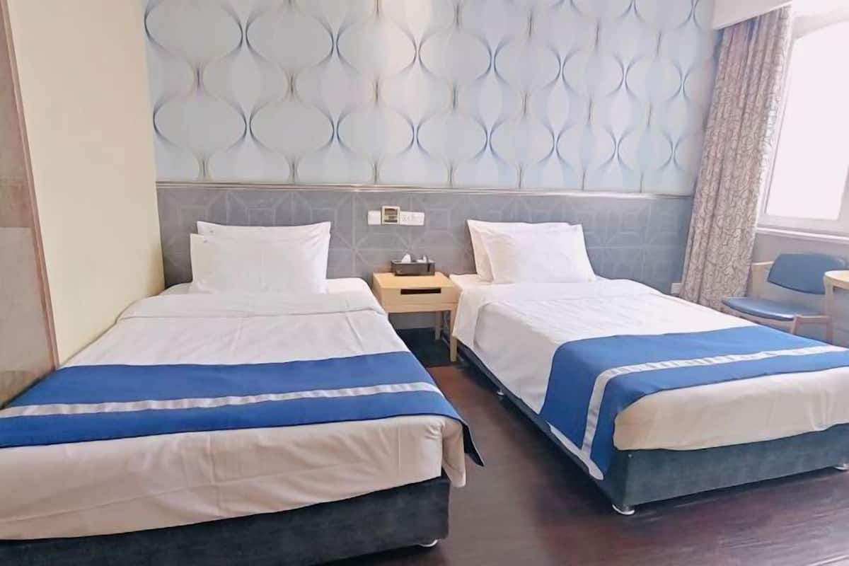 A hotel room with two beds, a nightstand, a small table, and a window with curtains.