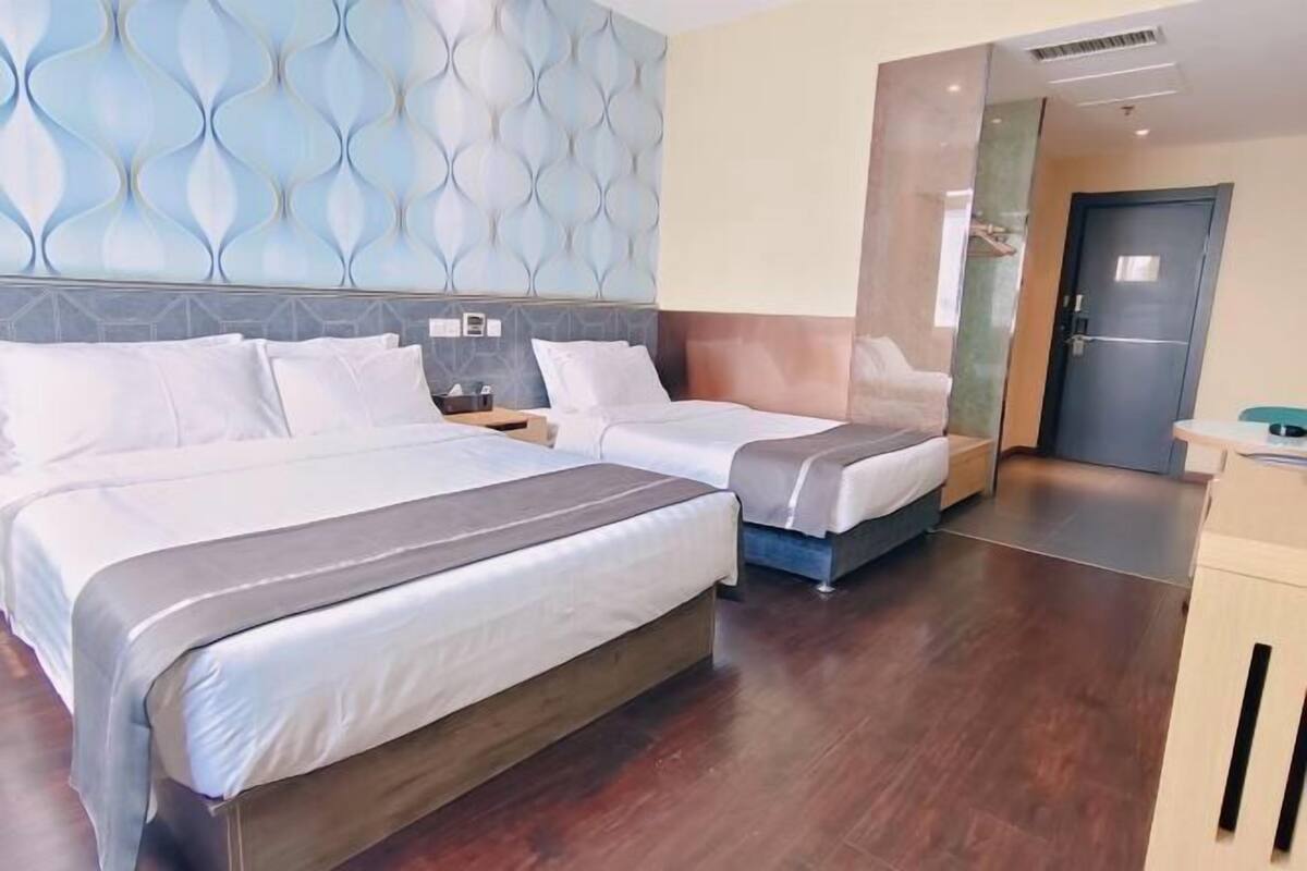 A hotel room with two beds, a modern wall design, a wooden floor, and a door to the right.