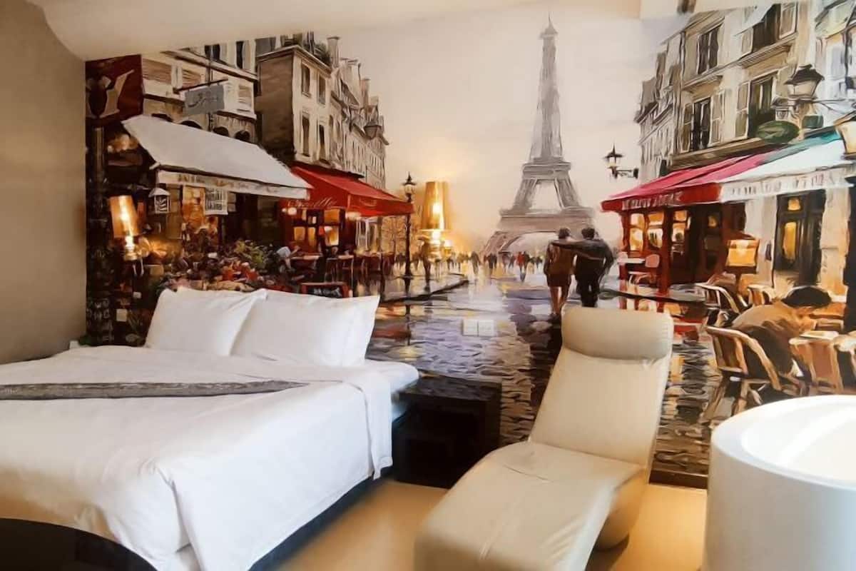 A hotel room with a bed, a chair, and a view of the Eiffel Tower through a mural.