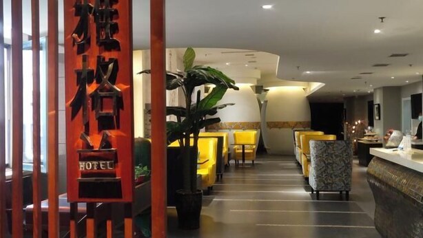 Un vestíbulo de hotel con mostrador de recepción, asientos amarillos y plantas en macetas.