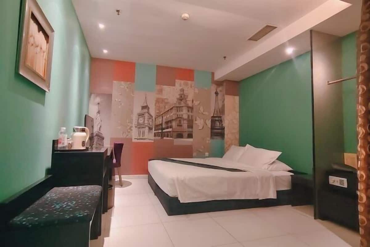 A hotel room with a bed, a desk, a chair, and a wall with a cityscape mural.