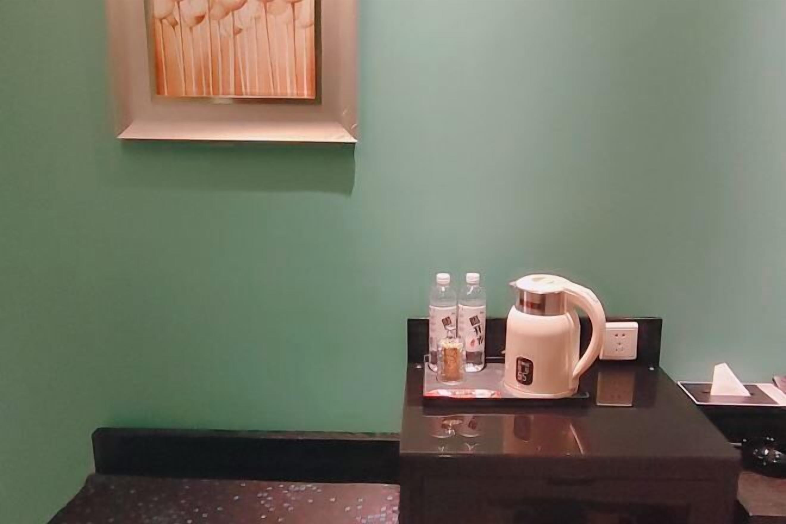 A hotel reception desk with a coffee machine, water bottles, and a framed artwork on the wall.