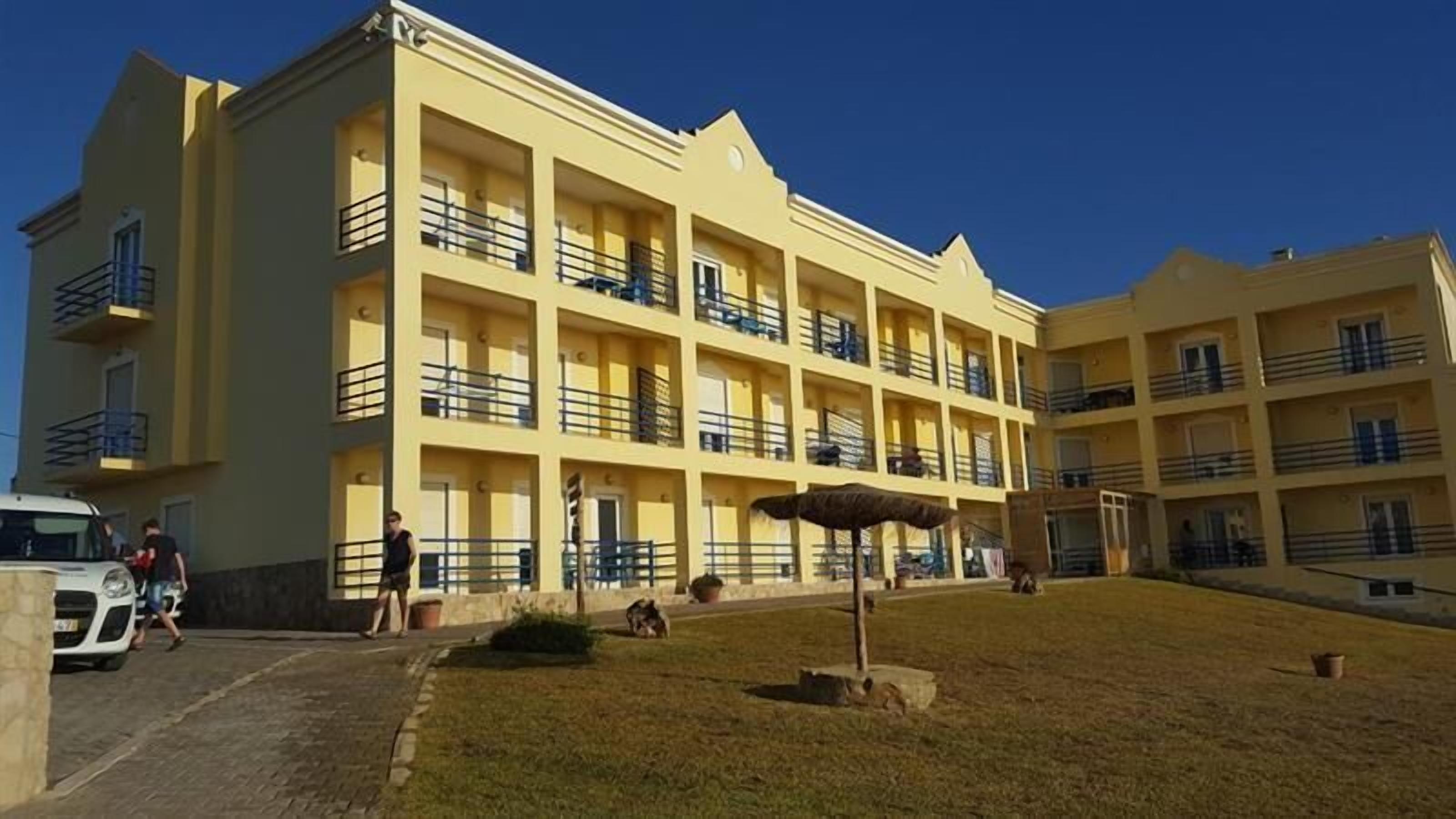 Ein mehrstöckiges Hotel mit Balkonen, einem gepflasterten Innenhof und einer Rasenfläche.