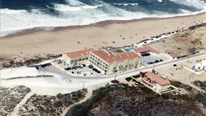 Vista aérea de um hotel à beira-mar, com vários edifícios, estacionamento e uma praia.