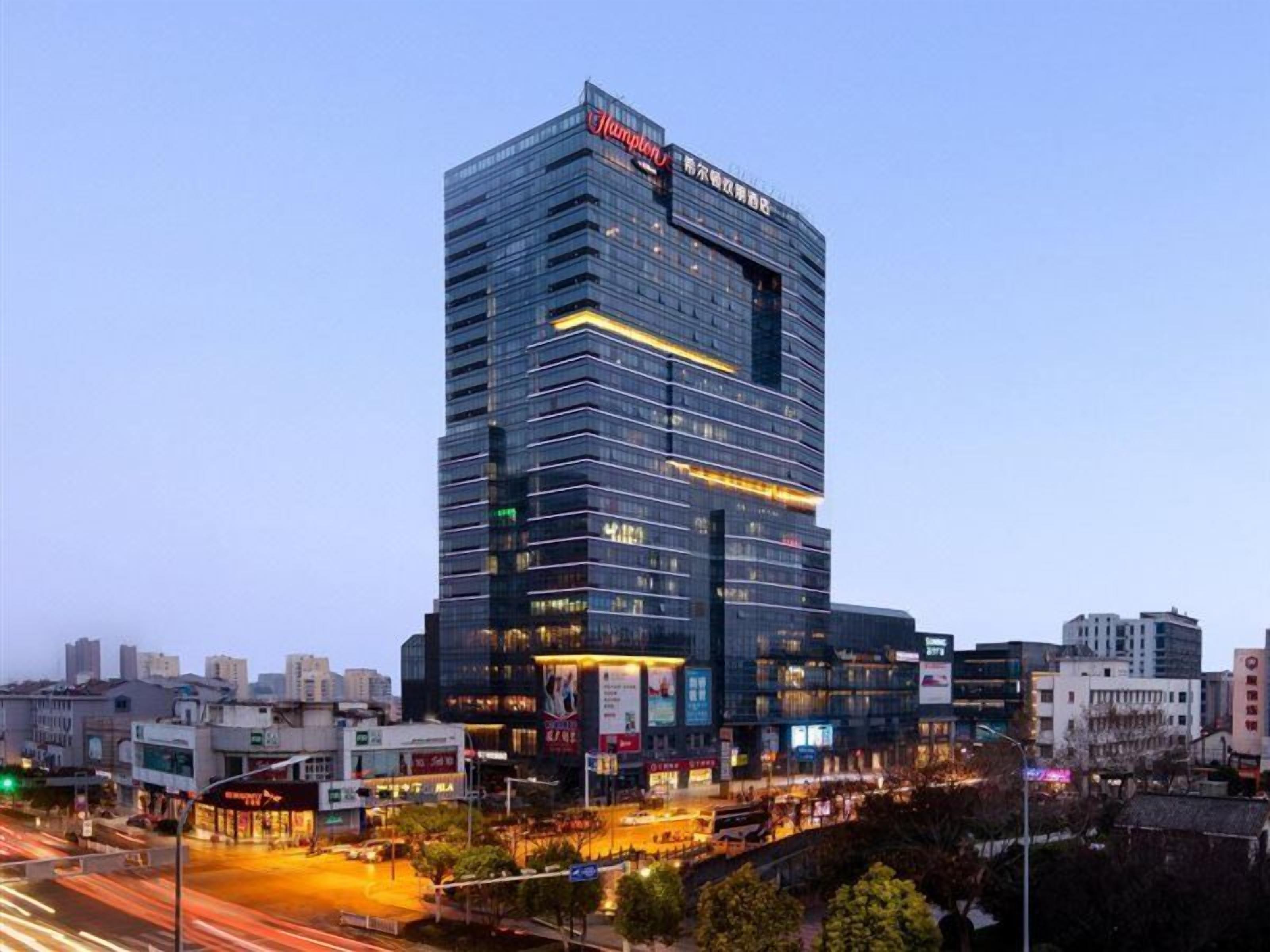 A modern high-rise building with a prominent sign at the top, surrounded by a busy urban street with visible traffic.
