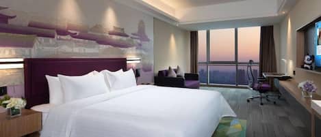 A hotel room with a large bed, a desk, a chair, and a view of the city.