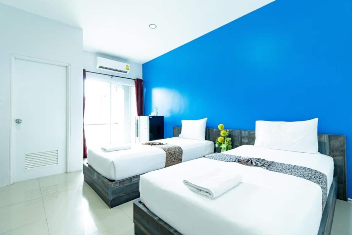 Una habitació d'hotel amb dos llits, una finestra amb cortines, un aparell d'aire condicionat i una porta.