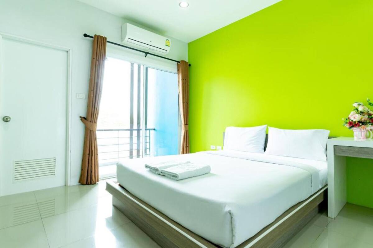 Habitació d'hotel amb un llit, una taula de nit, una finestra amb cortines i una paret de color verd clar.