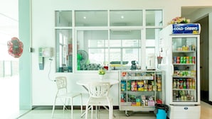 A room with a window, a fan, a table with chairs, and a refrigerator stocked with beverages. - Udee Living Place (Hat Yai)