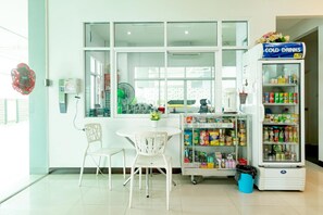 A room with a window, a fan, a table with chairs, and a refrigerator stocked with beverages. - Udee Living Place by Zuzu (Hat Yai)