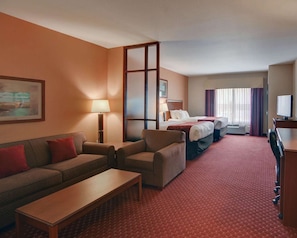 Hotellihuone, jossa on sohva, kaksi erillistä sänkyä, työpöytä, televisio ja suuri ikkuna, jossa on verhot.