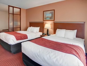 Hotellihuone, jossa on kaksi sänkyä, yöpöytä lampun kanssa, taulu seinällä ja liukuovi.