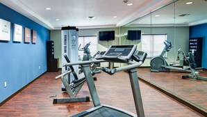 Une salle de sport d’hôtel équipée de tapis de course, de vélos elliptiques et d’un mur avec des miroirs.