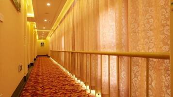 A hotel corridor with patterned carpet, a railing, and patterned curtains.